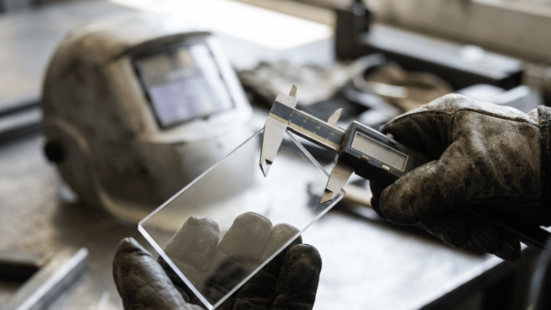 Hands measuring a clear welding helmet lens with calipers to confirm 2x4.25 size